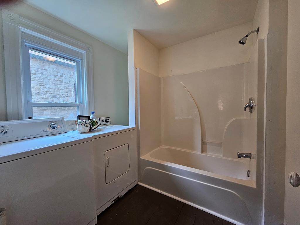 Bathroom with a bathtub and shower beside a washer and dryer under a window.