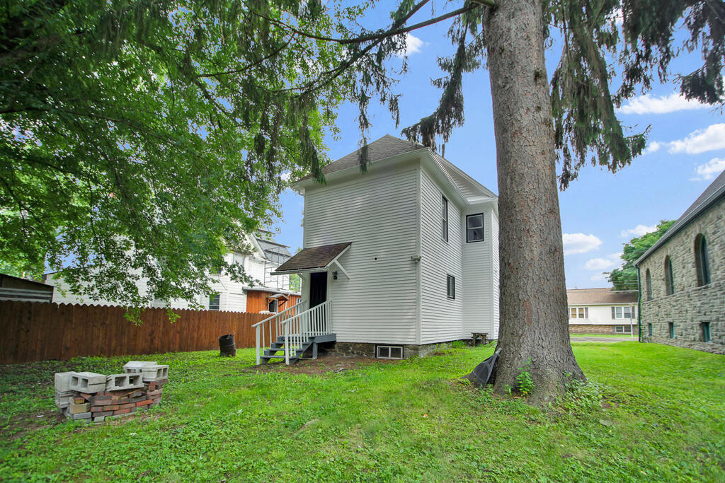White two-story house with a small porch and steps, partly screened by a large tree.