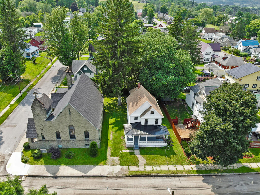 White two-story house with a covered porch and fenced yard beside a stone church.