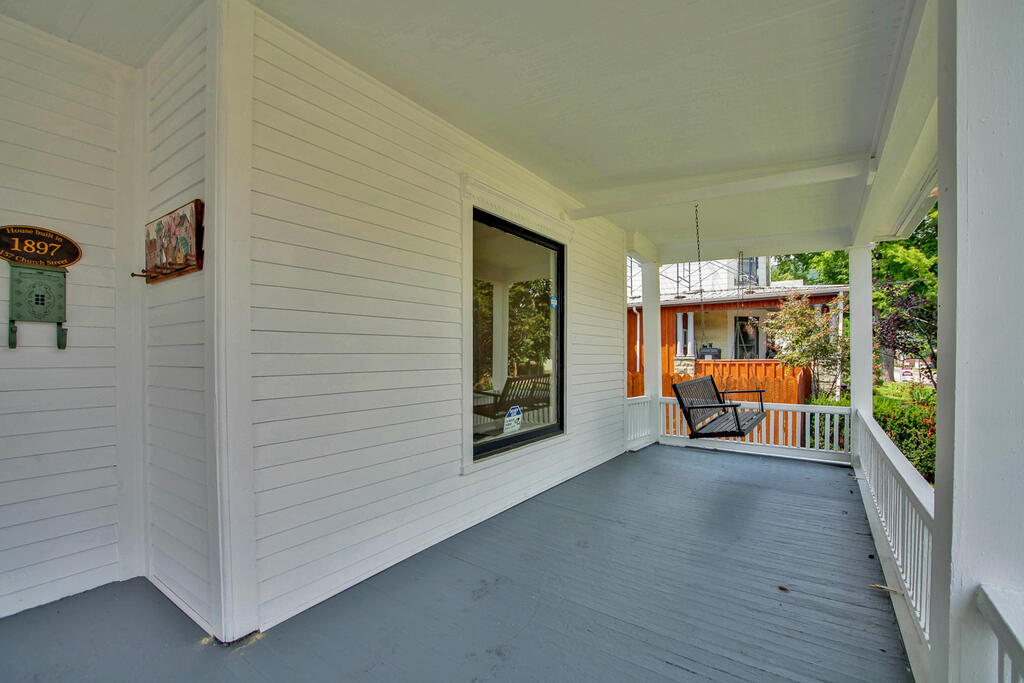 Covered porch with gray floorboards, white railings, and a black porch swing.