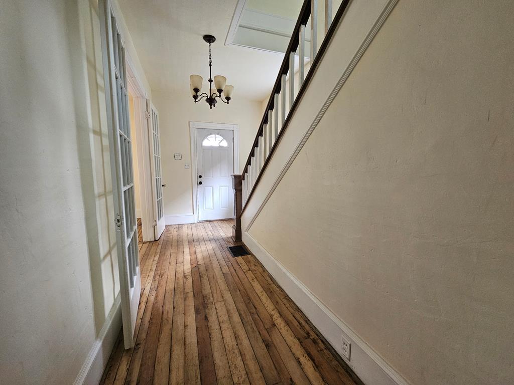 Entry hall with worn plank floors, a white arched-window door, and staircase.