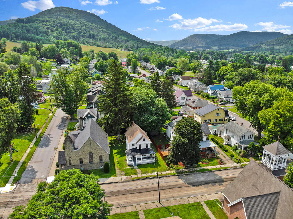 Aerial view of a small town beneath wooded mountains, with a stone church near the foreground.