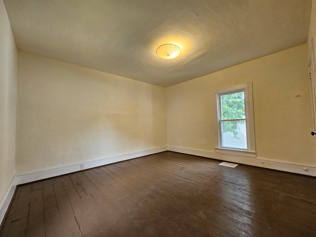 Empty room with dark hardwood floors, cream walls, and a single window.