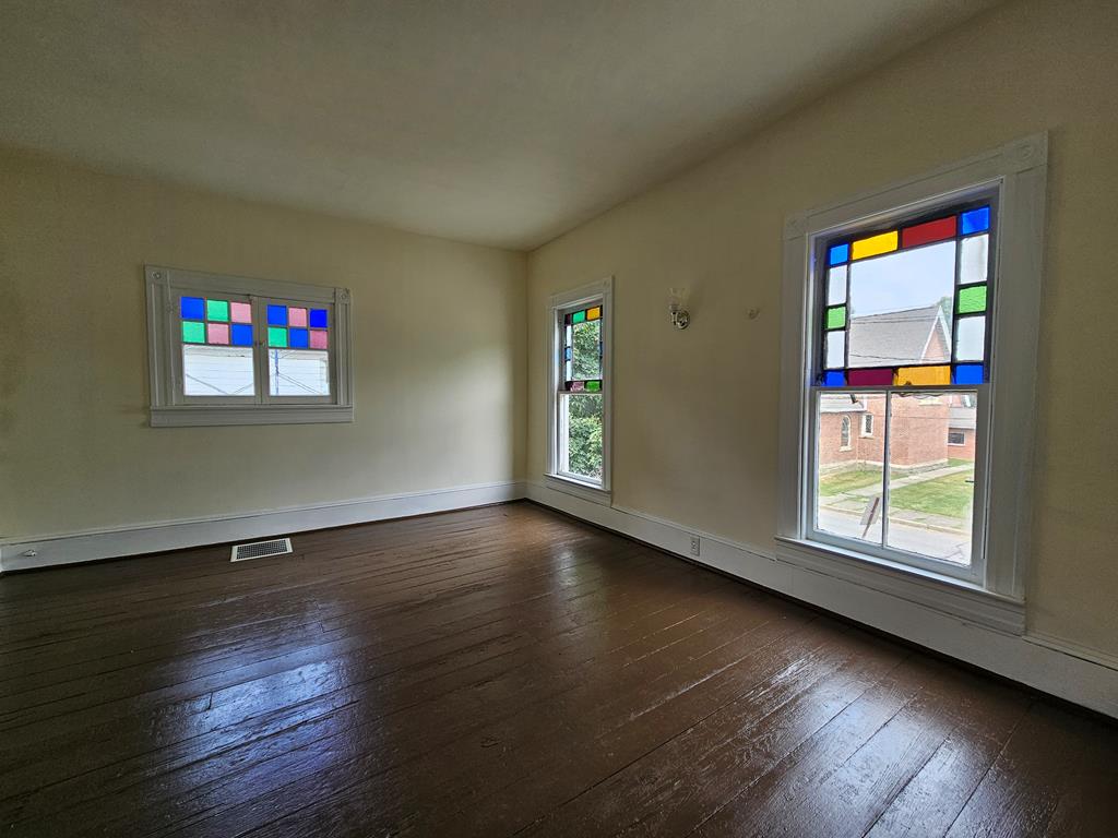 Empty room with dark hardwood floors and colorful stained-glass window panels.