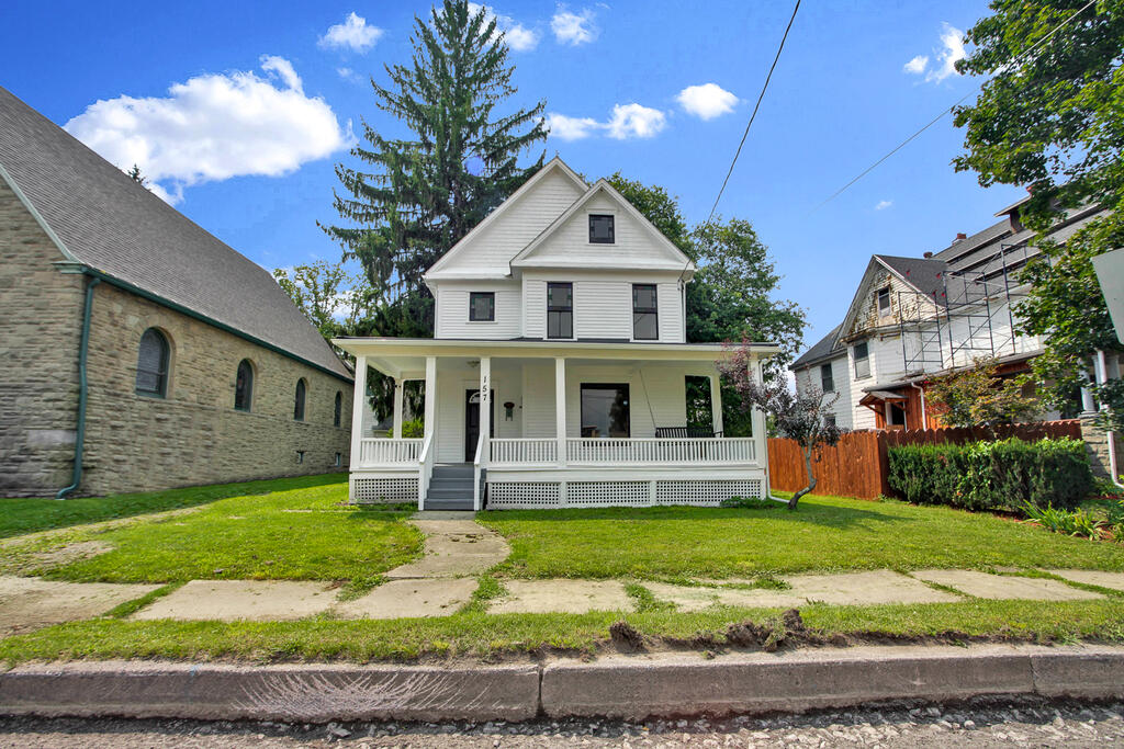 White two-story house with a broad covered porch, beside a stone church.