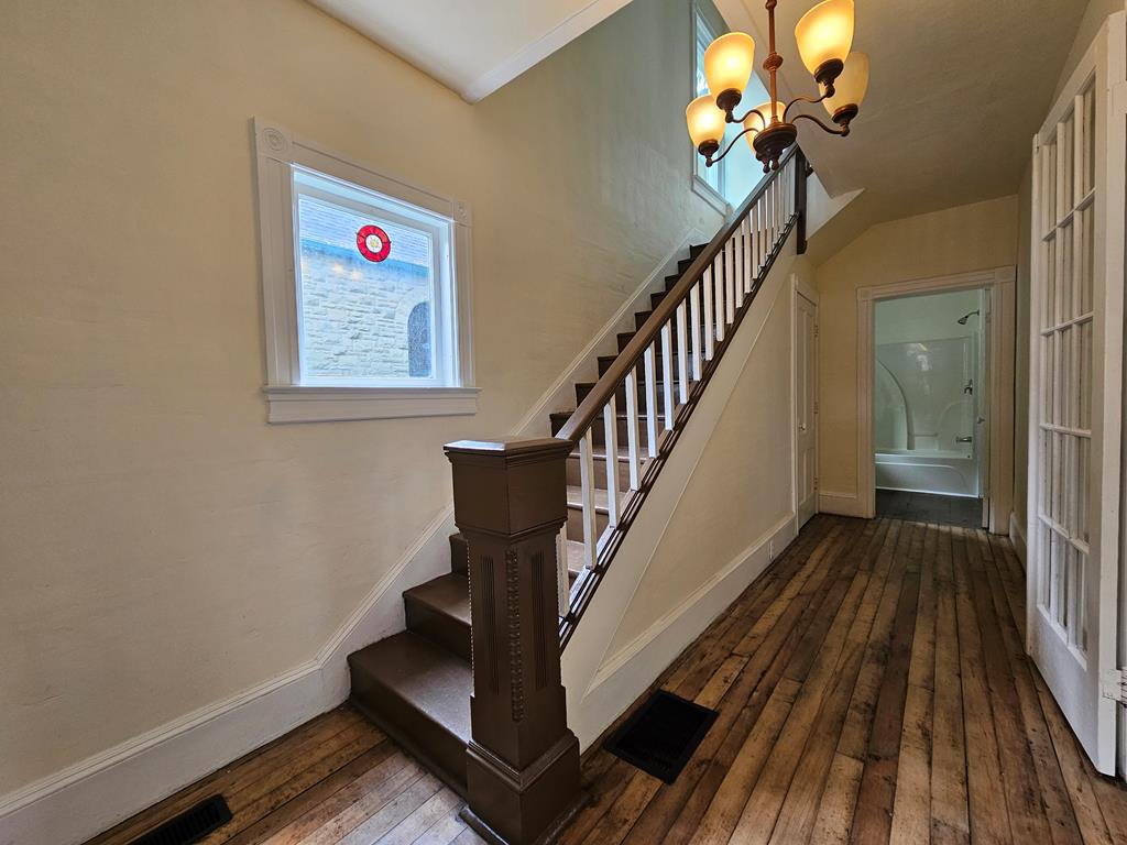 Hallway with a dark wood staircase, worn plank floors, stained-glass window, and chandelier.