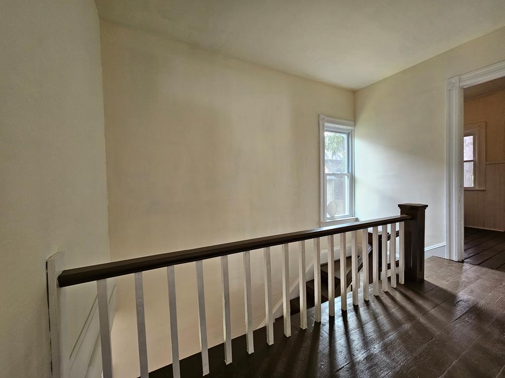 Upstairs landing with a dark wood floor, white stair railing, and narrow window.
