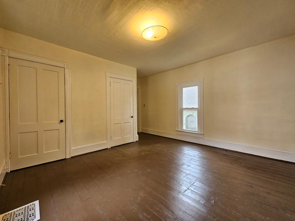 Vacant room with dark wood floors, cream walls, two paneled doors, and one window.