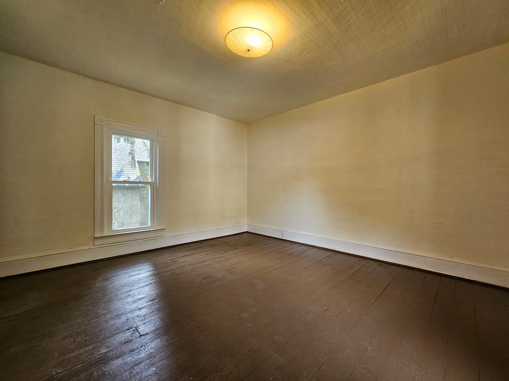 Vacant room with dark hardwood floors, beige walls, and a single window.