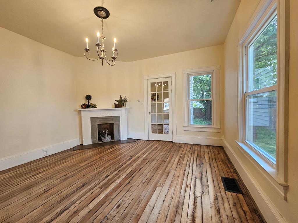 Living room with a white fireplace, exposed wood floors, chandelier, and tall windows.