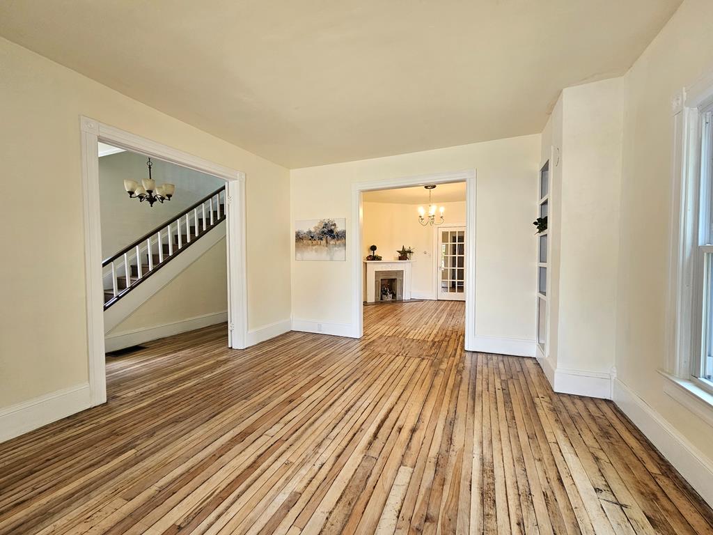 Empty room with exposed wood floors, a staircase through one doorway, and a fireplace beyond another.