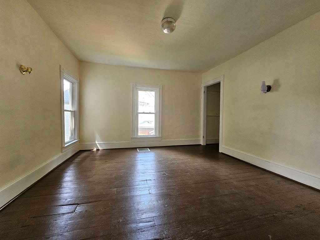Empty room with dark plank flooring, two windows, and an open doorway.