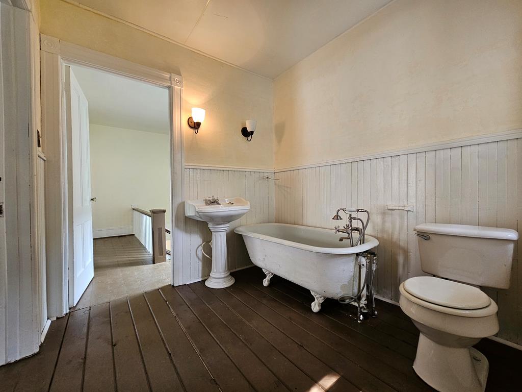 Bathroom with a clawfoot tub, pedestal sink, white wainscoting, and dark plank flooring.