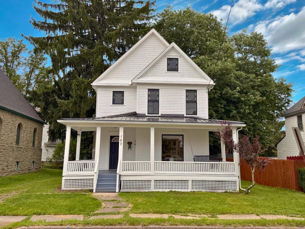 White two-story house with a wide covered porch, blue front door, and number 157 beside the entrance.