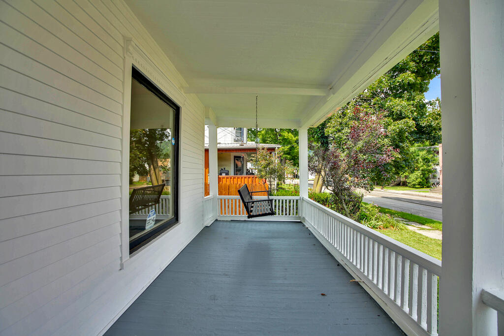 Covered front porch with gray decking, white railings, and a black rocking chair.