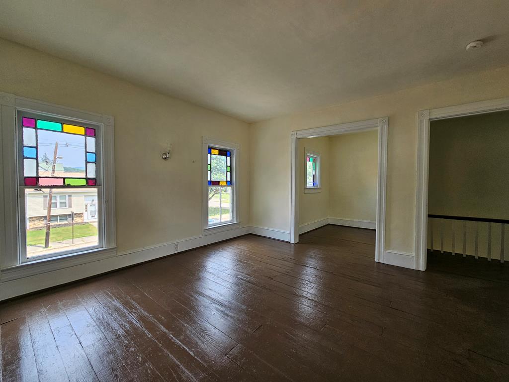 Empty room with dark hardwood floors, colorful stained-glass window panels, and wide doorways to adjoining spaces.