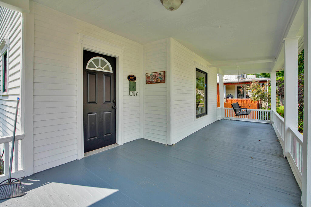 Covered front porch with gray floorboards, white railings, and a dark door marked 157.