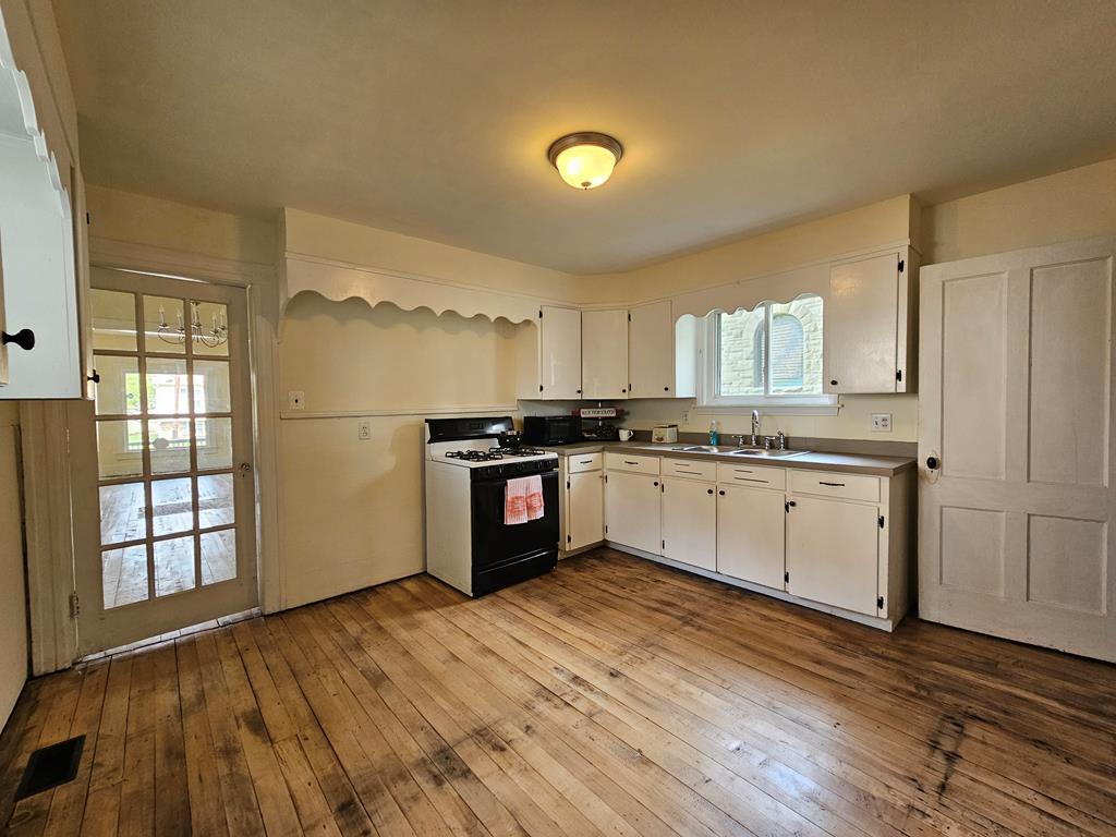 Kitchen with white cabinets, a black gas range, and worn hardwood floors.
