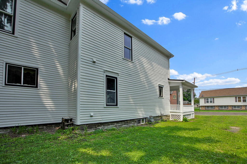 Two-story light-sided house with a small covered porch and green lawn.