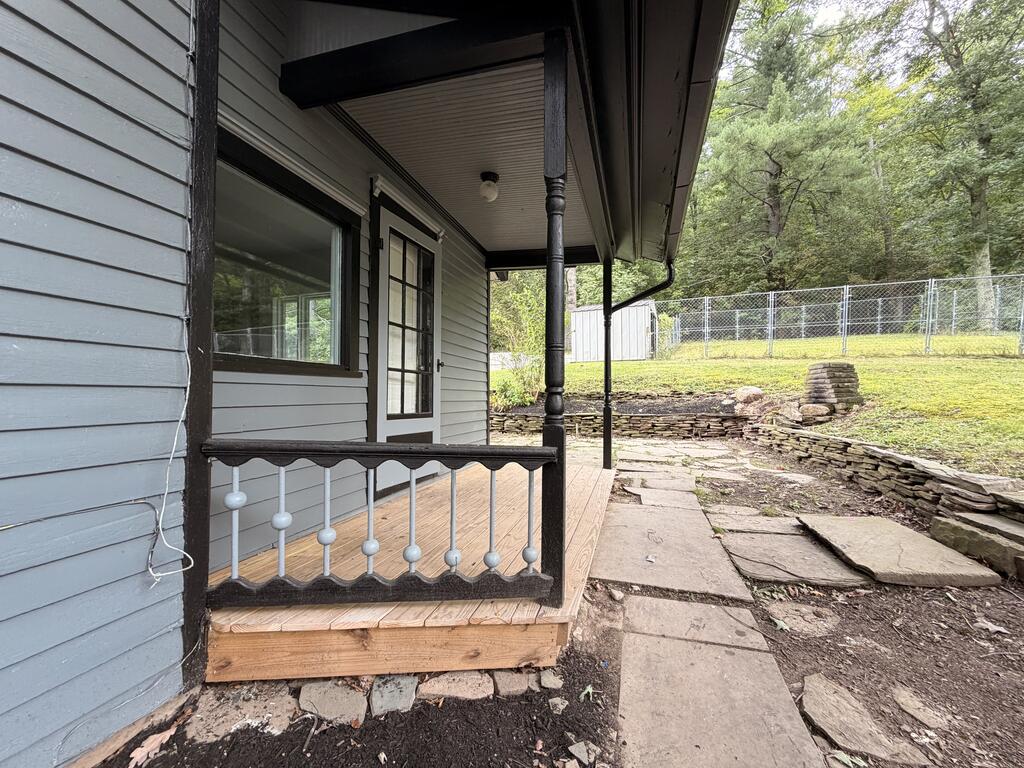 Gray-sided house with a covered porch beside a stone walkway and fenced yard.
