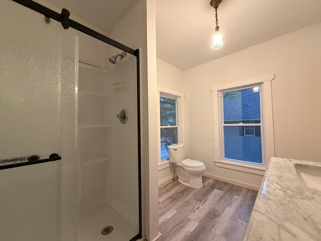 Bathroom with a glass shower, two windows, and a marble-look vanity.