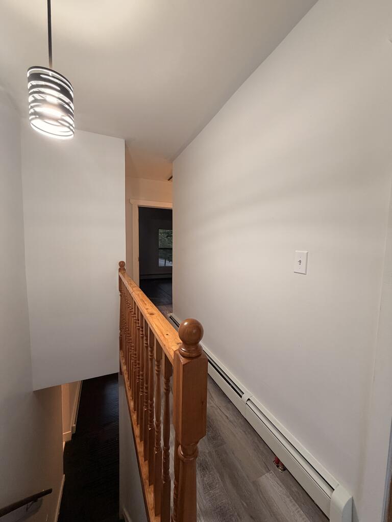 Hallway landing with a wooden stair railing, gray flooring, and a modern pendant light.