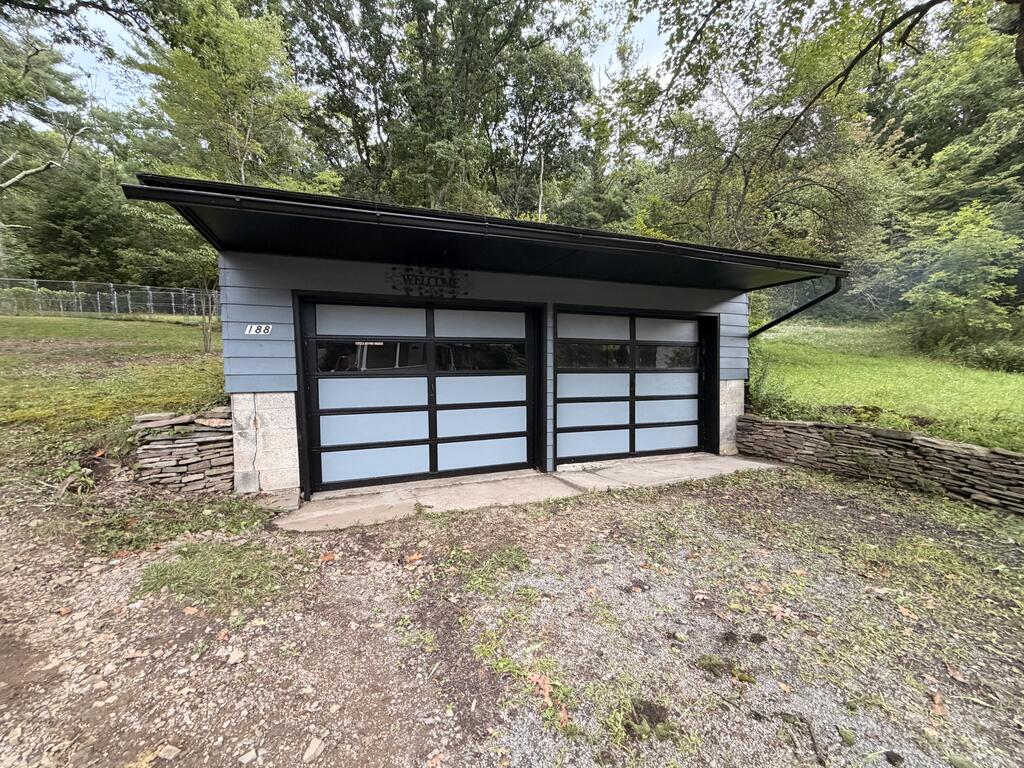 Detached two-door garage with blue-gray siding and a broad black roof, surrounded by trees.
