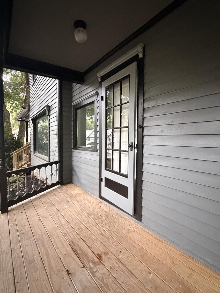 Covered wooden porch with gray siding, a glass-paneled door, and decorative railing.