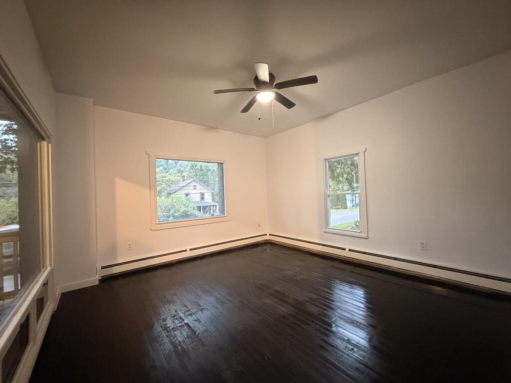 Empty room with dark hardwood floors, several windows, and a ceiling fan.