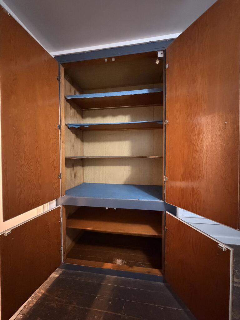 Open wooden cupboard with empty shelves and a wide blue-gray shelf.