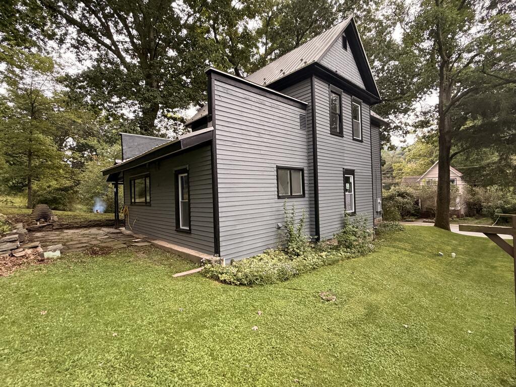 Gray two-story house with a steep metal roof, black trim, and a tree-shaded lawn.