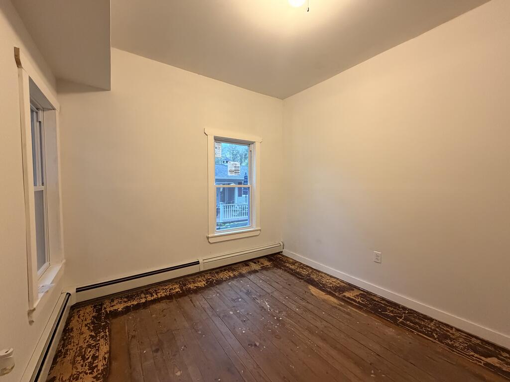 Empty room with worn dark wood floors, two windows, and baseboard heaters.