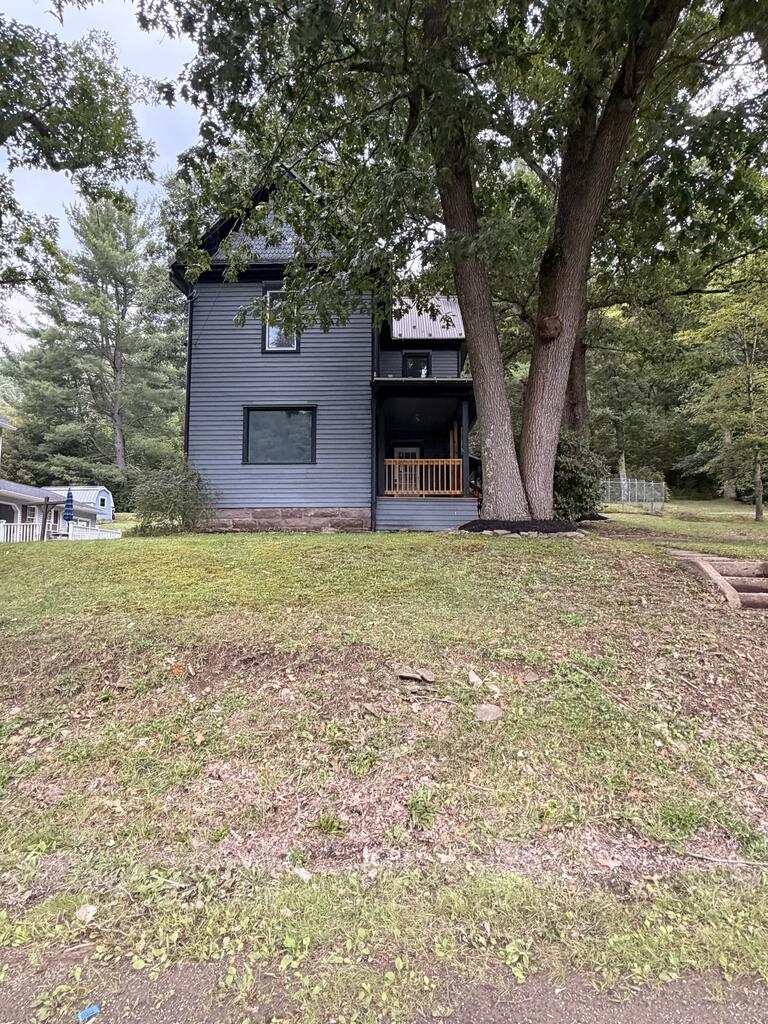 Gray two-story house with a covered porch, framed by large mature trees.