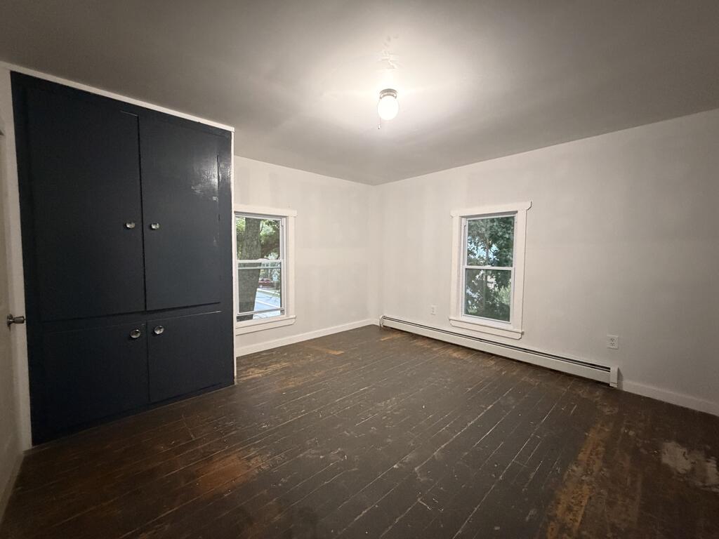 Vacant room with dark built-in cabinets, worn wood floors, and two windows.