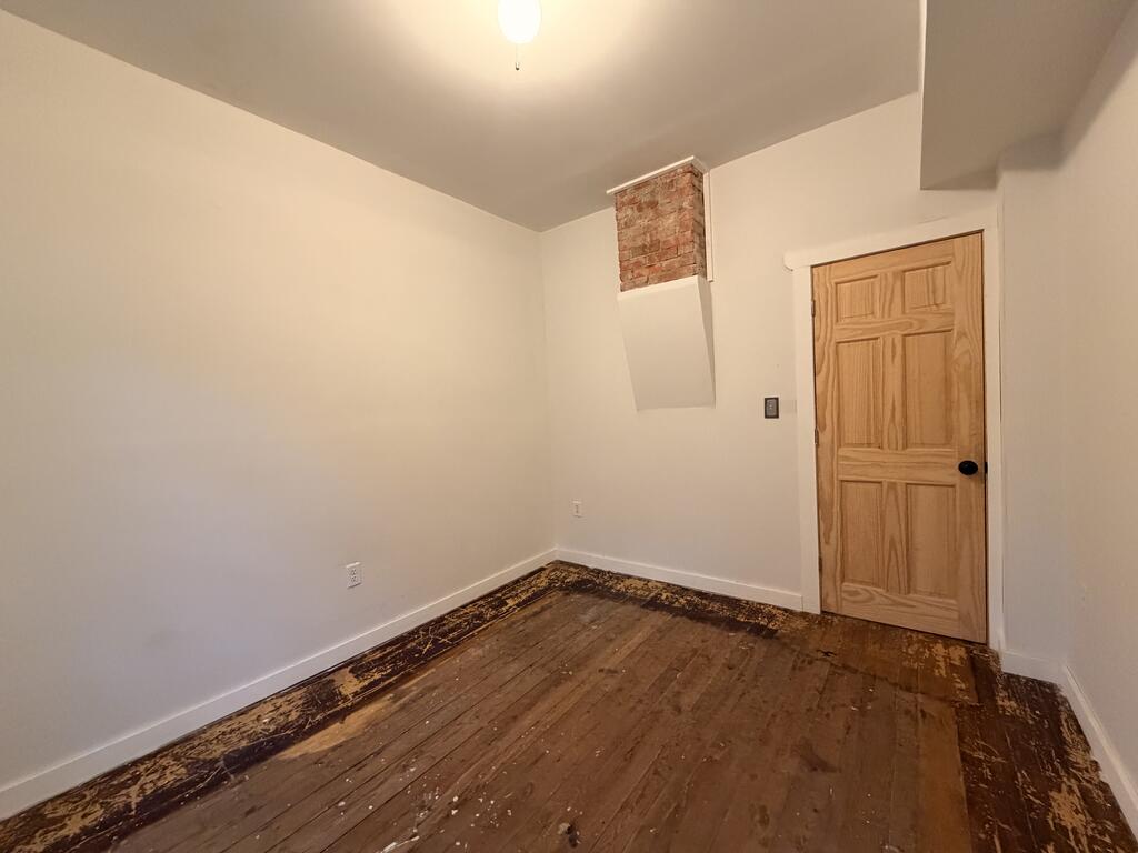 Empty room with a wooden door, exposed brick, and worn wood flooring.