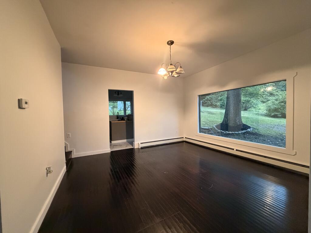 Empty living room with dark hardwood floors and a large window overlooking a tree-lined yard.