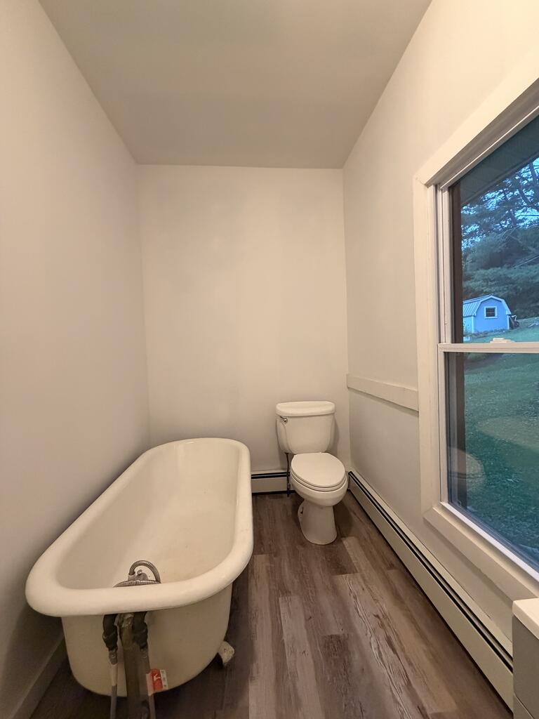 Bathroom with a freestanding tub beside a toilet and large window.