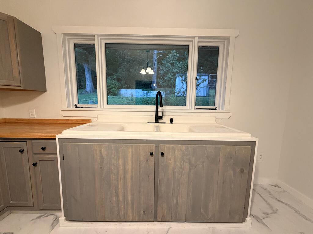 Kitchen with a farmhouse sink beneath a wide window, gray cabinets, and butcher-block counter.