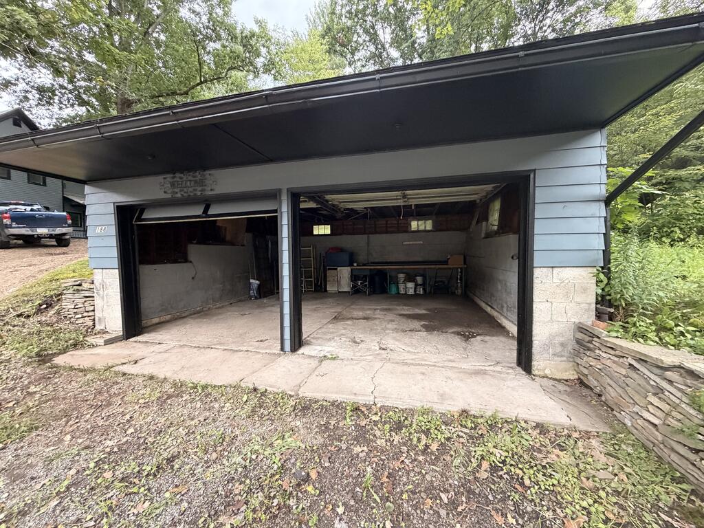Two-bay garage with both doors open, a broad overhanging roof, and storage along the back wall.