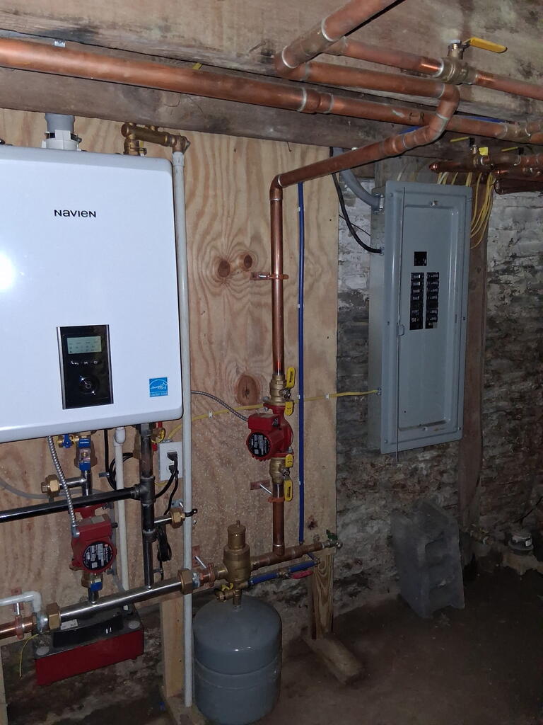 Basement mechanical room with a Navien boiler, copper pipes, and electrical panel.
