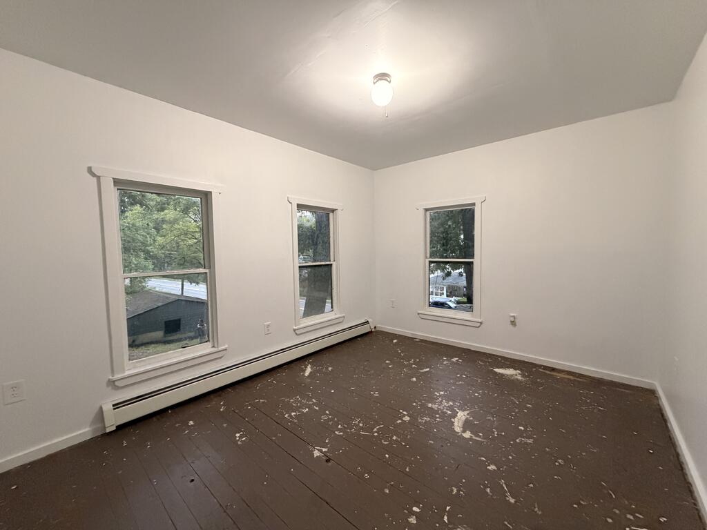 Empty room with three windows and a scuffed dark wood floor.