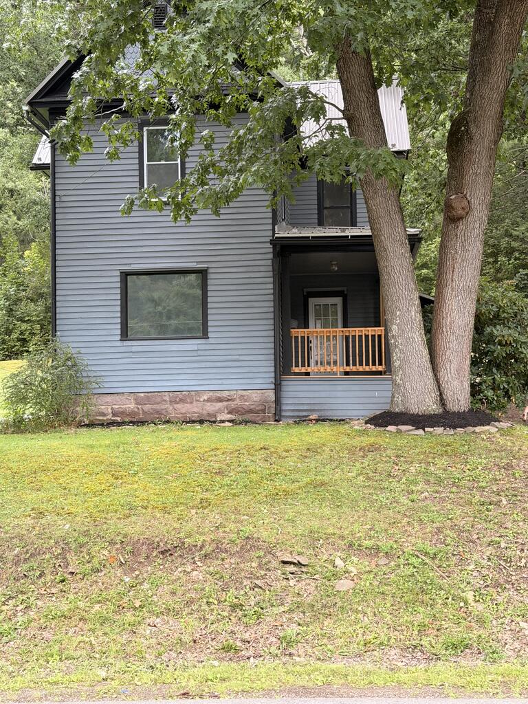 Two-story gray house with a covered porch, partly shaded by mature trees.