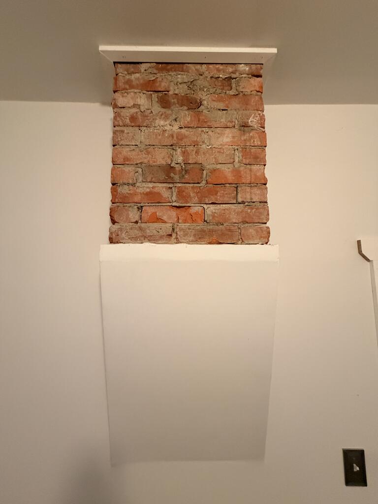 Exposed red brick section above a white-painted wall projection.