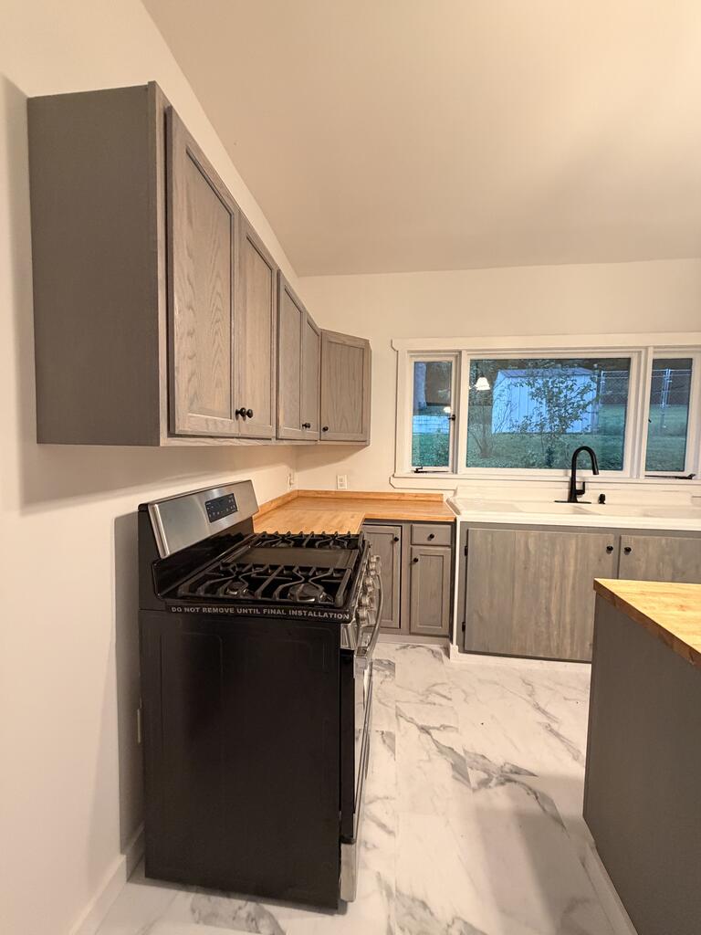 Kitchen with gray cabinets, a black gas range, and farmhouse sink beneath a wide window.