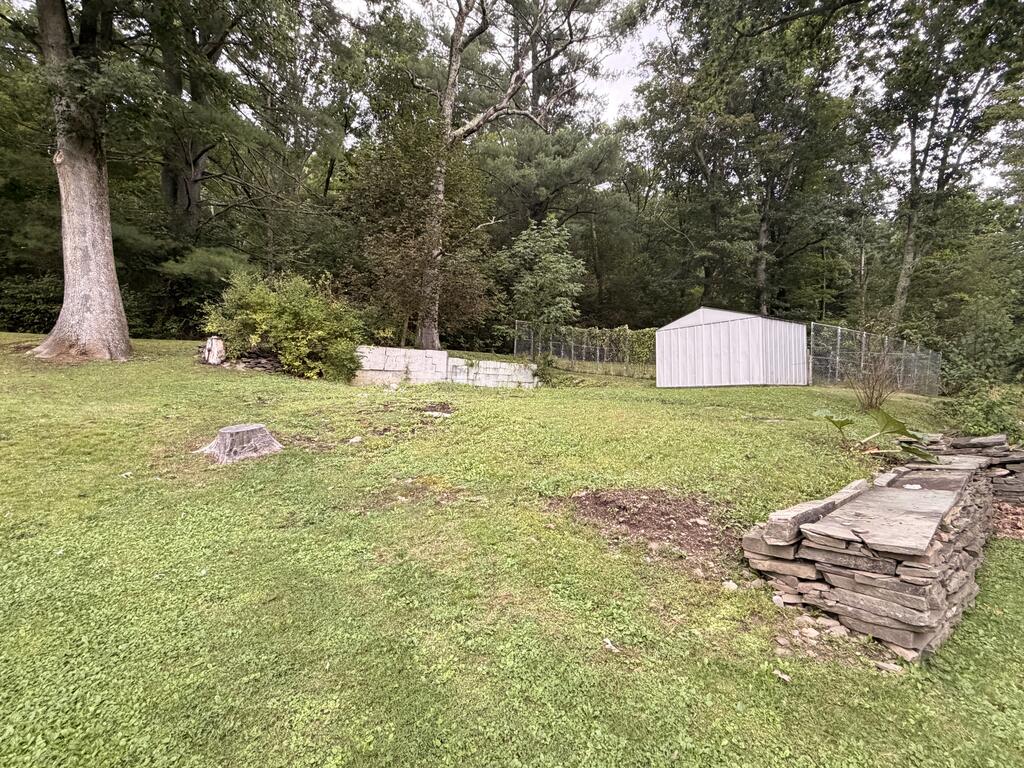 Backyard with a white shed, chain-link fence, mature trees, and stacked-stone wall.
