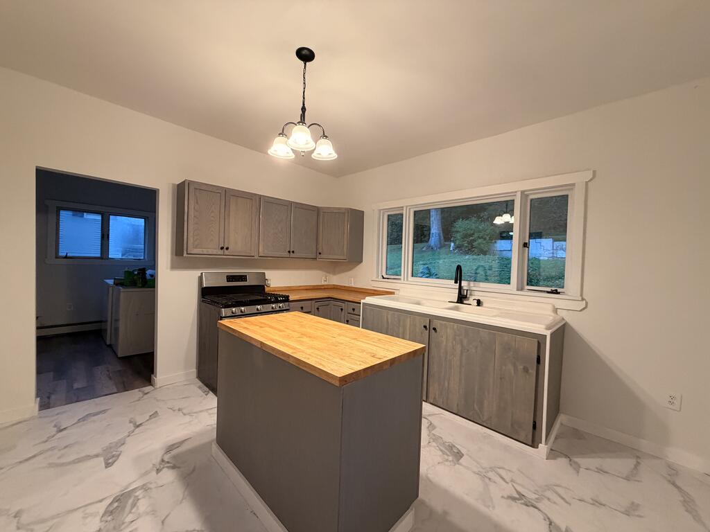 Kitchen with gray cabinets, a wood-topped island, and a sink beneath a wide window.