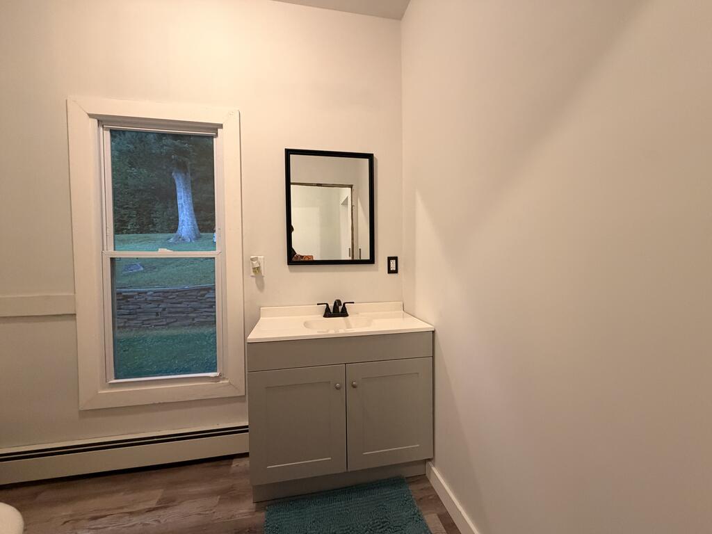 Bathroom with a gray vanity and mirror beside a window overlooking a lawn and stone wall.