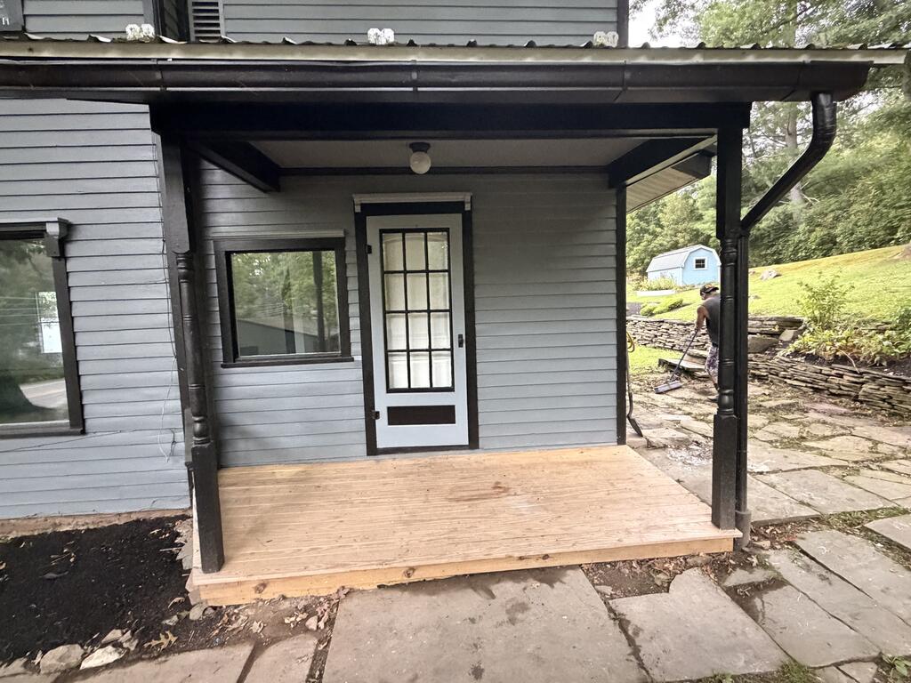 Covered front porch with gray siding, black trim, a new wooden deck, and a stone path.