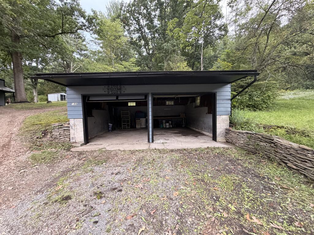 Detached two-bay garage with open doors, blue siding, and stone lower walls.