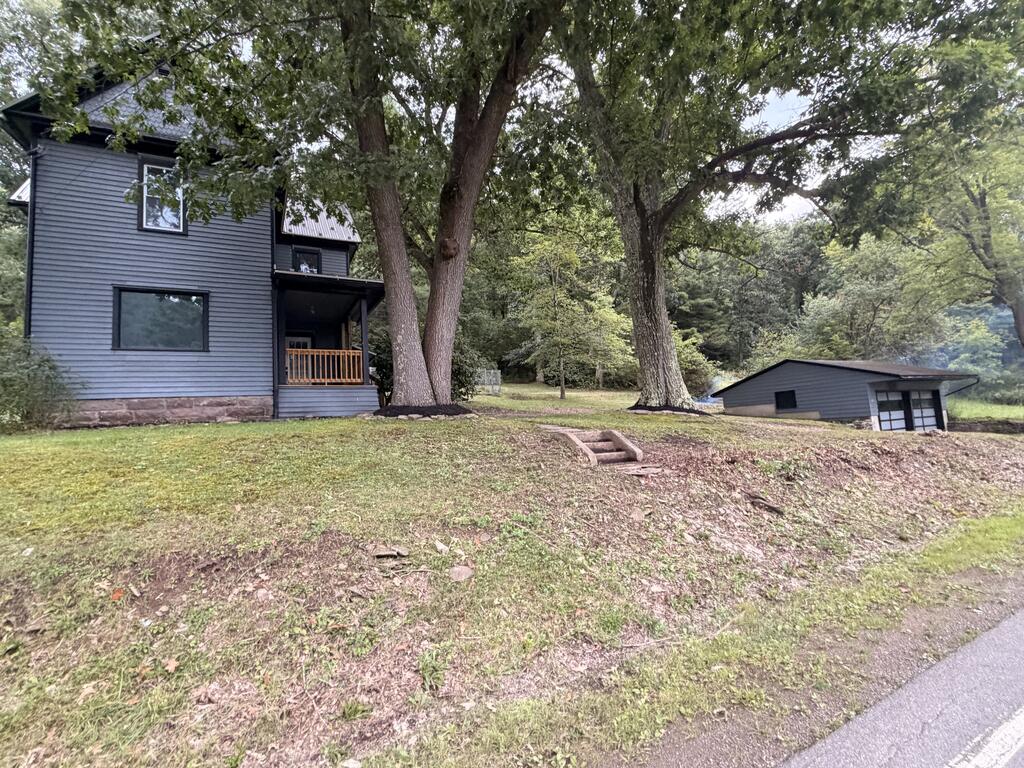 Gray two-story house with a covered porch, mature trees, and a detached garage.